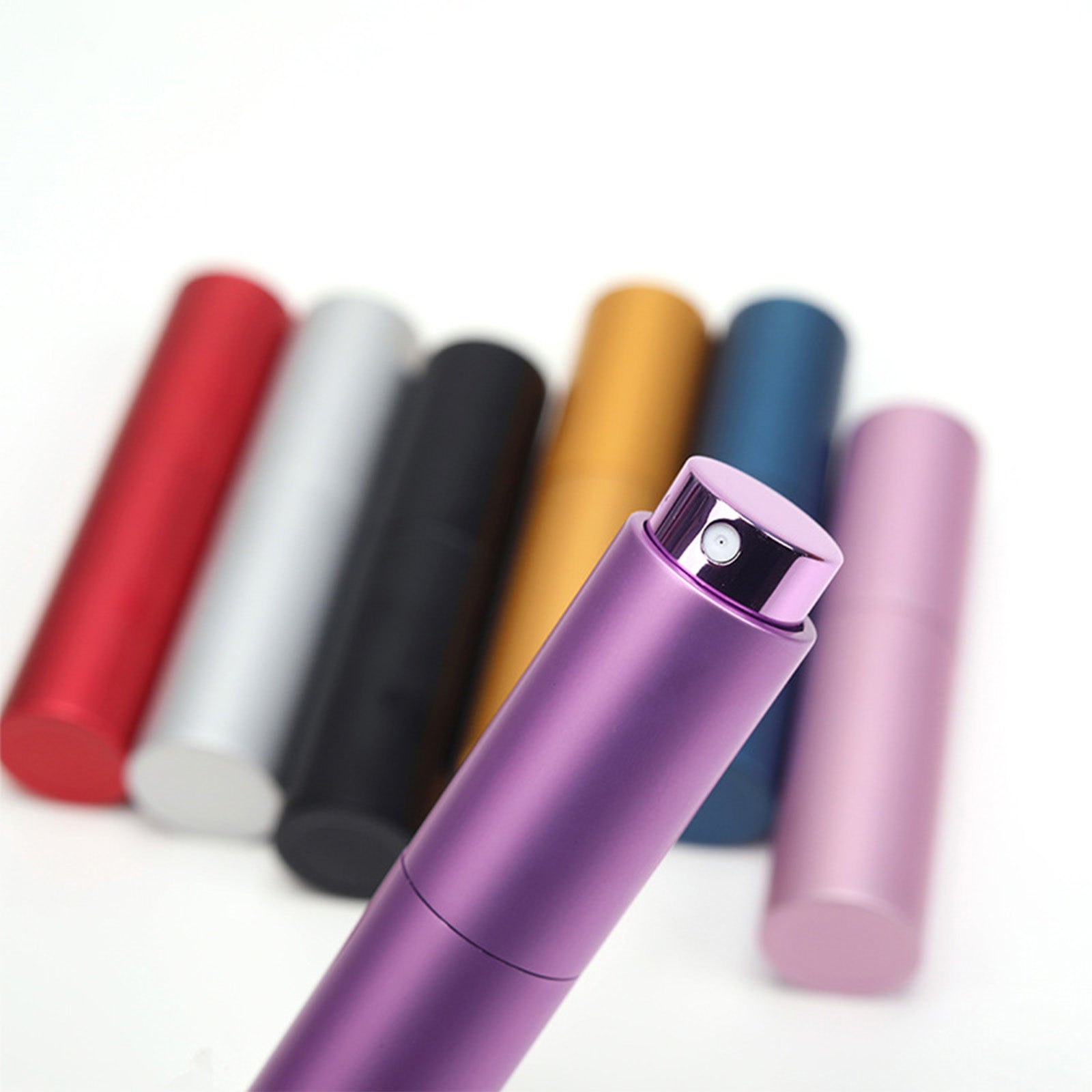 Close-up image of a purple cylindrical perfume spray bottle with a black nozzle. In the background, there are six more cylindrical bottles in red, silver, black, gold, blue, and pink, slightly out of focus. The backdrop is plain white. The sleek design could be achieved using a CrealityFalcon 10pcs Portable 8ml Atomizer Perfume Spray Bottle for Laser Engraving.