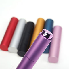 Close-up image of a purple cylindrical perfume spray bottle with a black nozzle. In the background, there are six more cylindrical bottles in red, silver, black, gold, blue, and pink, slightly out of focus. The backdrop is plain white. The sleek design could be achieved using a CrealityFalcon 10pcs Portable 8ml Atomizer Perfume Spray Bottle for Laser Engraving.