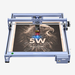 A CrealityFalcon CR-Laser Falcon 10W laser engraver in action, etching a detailed image of an eagle on a wooden surface. The machine has a blue metallic frame, and the high precision engraving area is centered beneath the laser module, which is actively working.