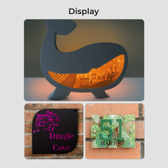 A display includes: a whale-shaped lamp crafted from engraver materials with an illuminated village scene; a sign featuring a purple dragon head and "Dingle Cove"; and a green plaque, made using Creality Falcon's frosted colorful acrylic sheets, displaying "51" and "Harvest.