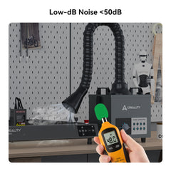 A person uses a decibel meter reading 48.0 dB to demonstrate the low noise operation of the Creality Air Purifier for 10W Engraving Machines by Creality Falcon, featuring a flexible hose. A pegboard with tools and a model is visible in the background. Text above states "Low-dB Noise <50dB.