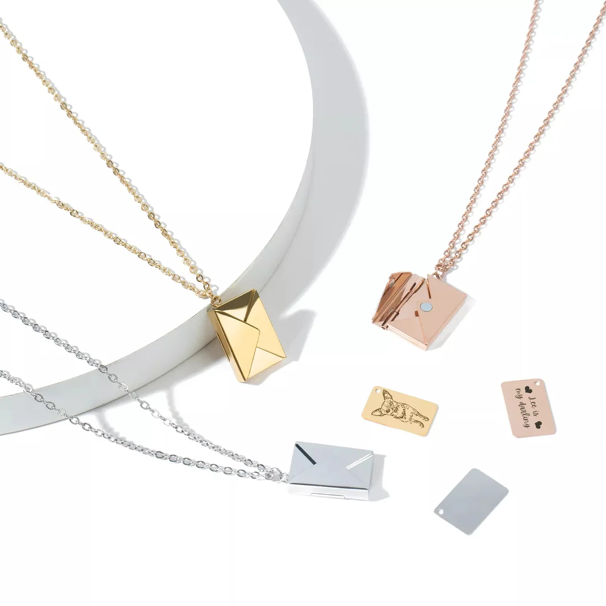 Two stainless steel Love Letter Envelope Necklaces from Creality Falcon, featuring envelope-shaped pendants in gold and silver, are elegantly displayed. Each piece includes a matching rectangular charm and a magnetic clasp for easy wear. They are beautifully arranged on a circular white backdrop.