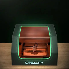 A Creality Falcon 3D printer from the Air Purifier Bundle, featuring a transparent top and green accent lights, is on display. It offers quiet functionality with low-noise operation, all while showcasing its interior printing mechanism.