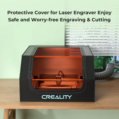 A Creality Falcon Falcon2 22W Laser Engraver and Cutter Ultimate Engraving Package, featuring a transparent orange protective cover, is positioned on a wooden desk. This cover not only enhances colorful engraving but also displays its powerful 22W cutting ability. A ventilation hose is connected for added safety. Above it, text reads: "Protective Cover for Laser Engraver—Enjoy Safe and Worry-free Engraving & Cutting.