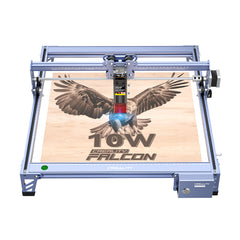 A CR-Laser Falcon 5W Laser Engraver from CrealityFalcon is shown in operation. The machine, known for its ultra-fine engraving precision, is etching an image of an eagle with wings spread wide on a wooden surface. The text "5W" and "CR-Laser Falcon" appear below the eagle on the wood.