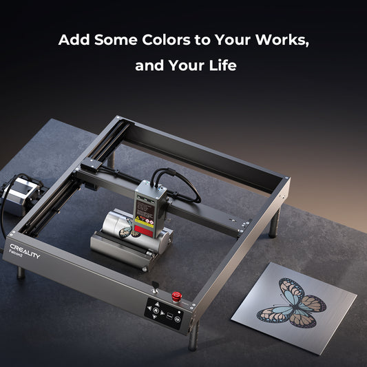 A CrealityFalcon Falcon2 40W Laser Engraver and Cutter is displayed on a dark surface. Next to it lies a metal plate with an engraved, multicolored butterfly design. Above the scene, text reads, "Add Some Colors to Your Works, and Your Life." The advanced safety measures ensure a secure creative process.