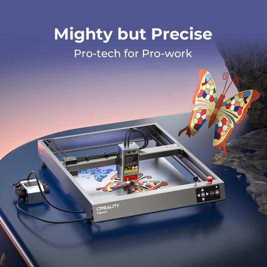 Top view of a CrealityFalcon Falcon2 40W Laser Engraver and Cutter. The machine is crafting two colorful mosaic butterfly designs on a metal sheet. The surrounding frame and mechanical components are visible, with a control box on the left connected by cables. 1000